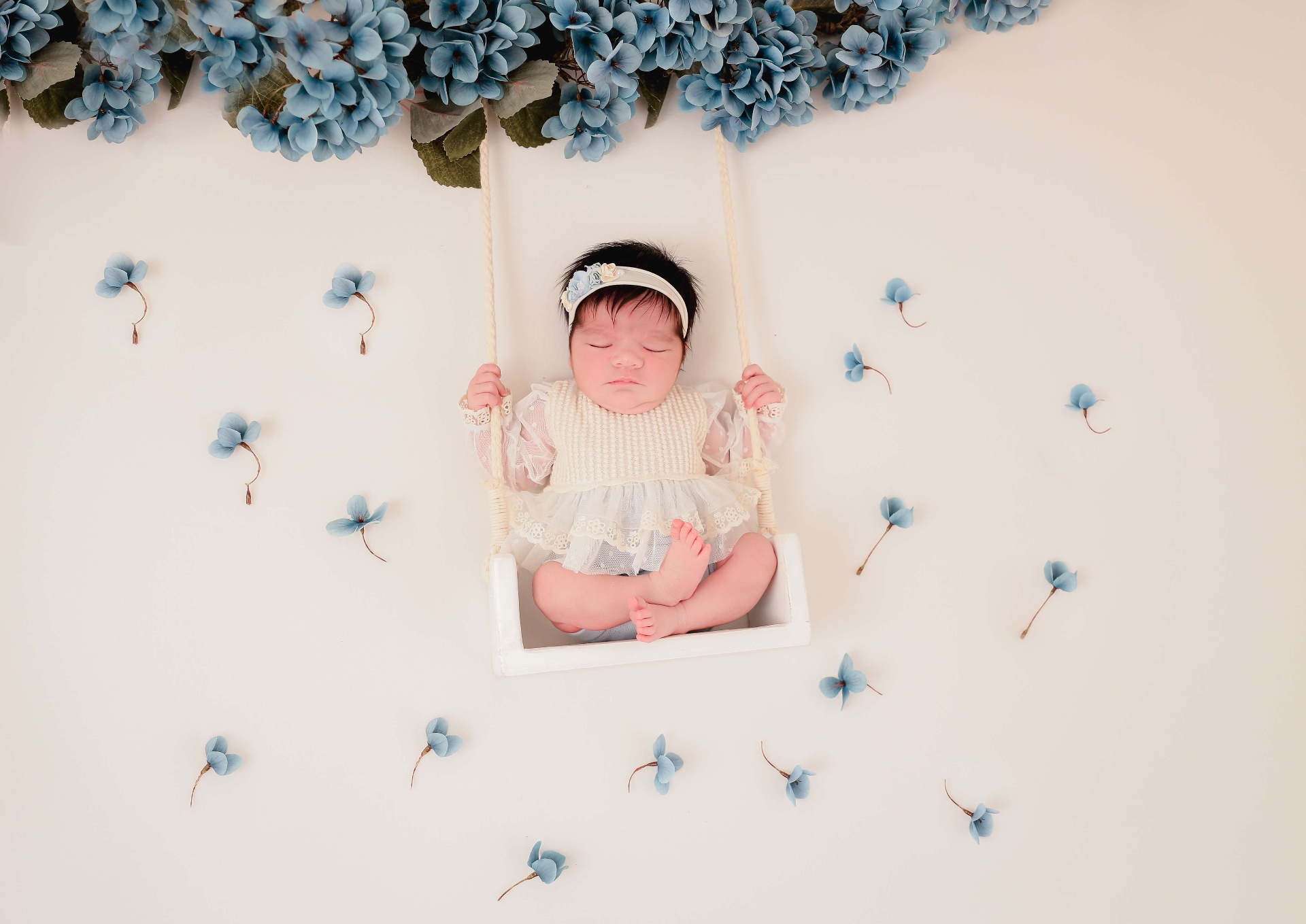 Bebê em balanço com flores azuis ao redor